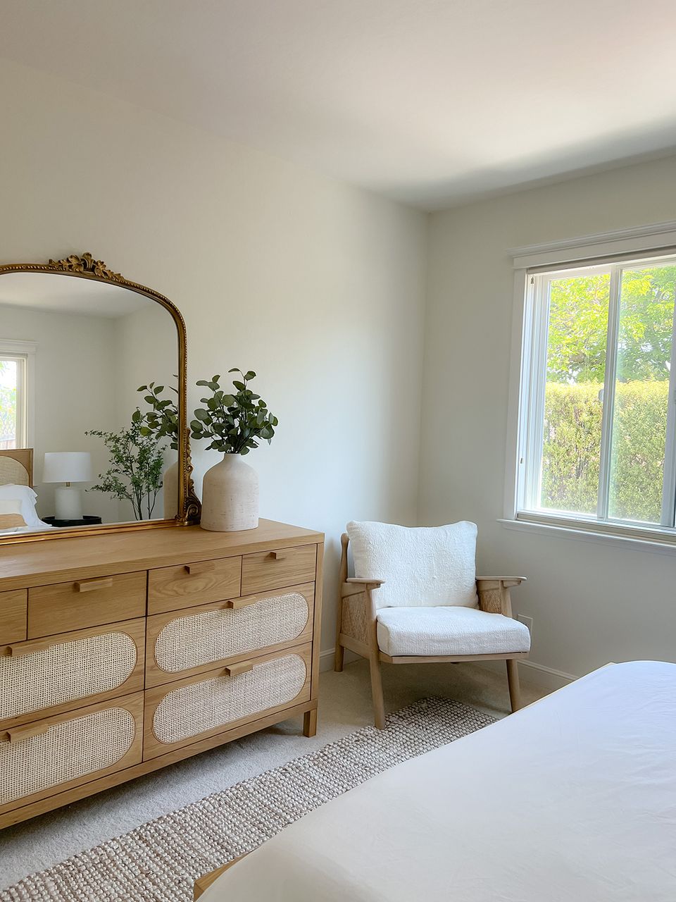 Peaceful organic modern corner with wood dresser, arched mirror, cream chair, and soft natural light