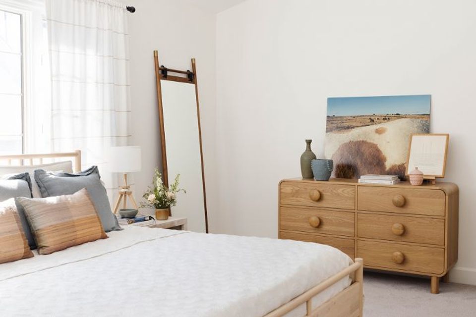 Serene mid-century bedroom with warm wood dresser, simple landscape art, and uncluttered aesthetic