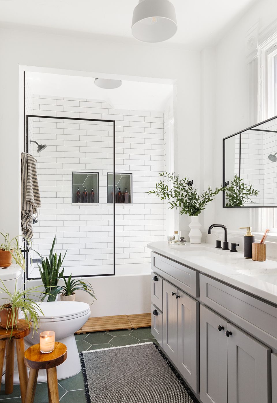 Bright, airy bathroom with white subway tile, soft gray cabinetry, black-framed shower, and warm wood accents for a clean, modern farmhouse feel.