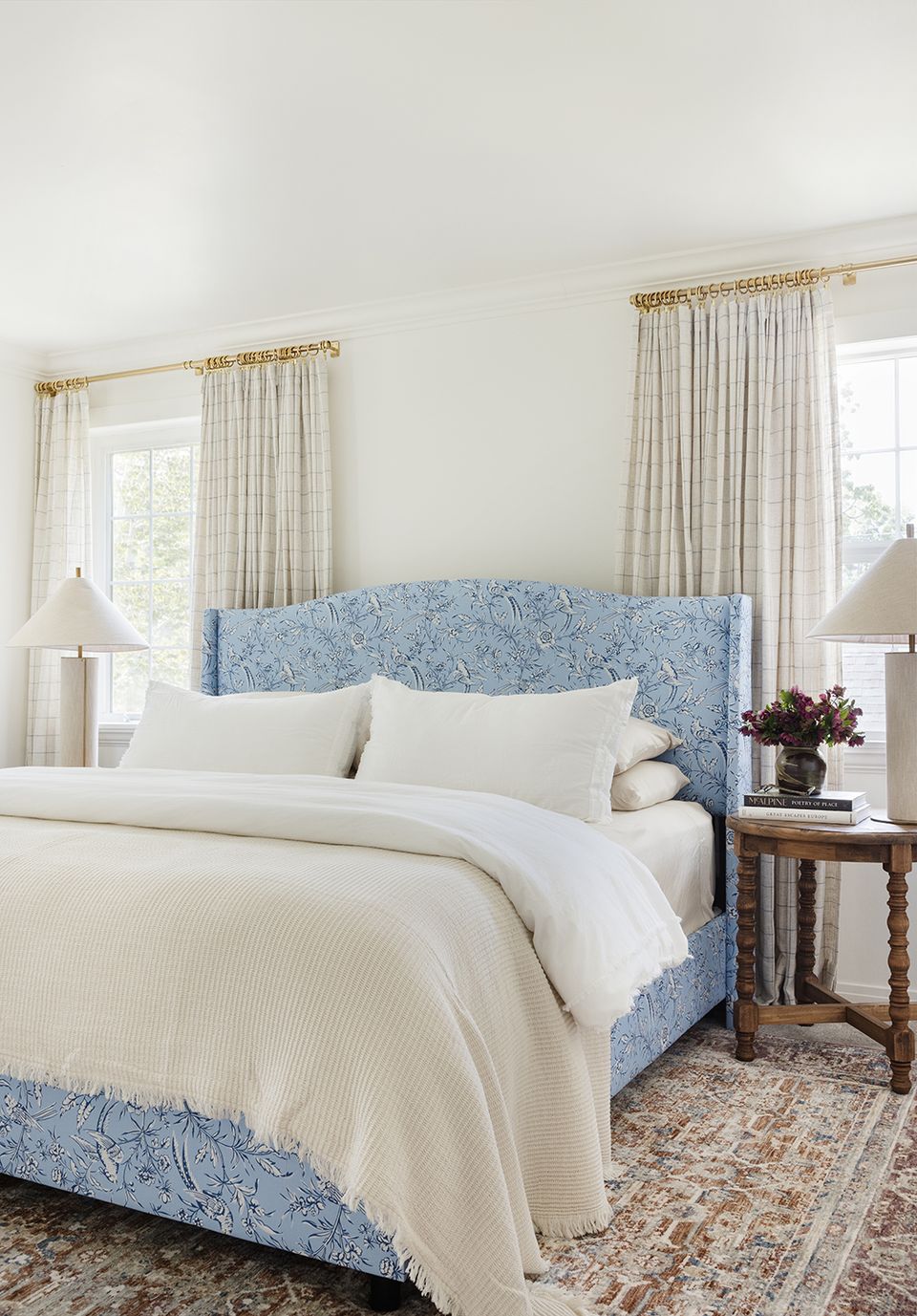 Classic bedroom with blue patterned headboard, cream bedding, brass curtain rods, and serene color palette
