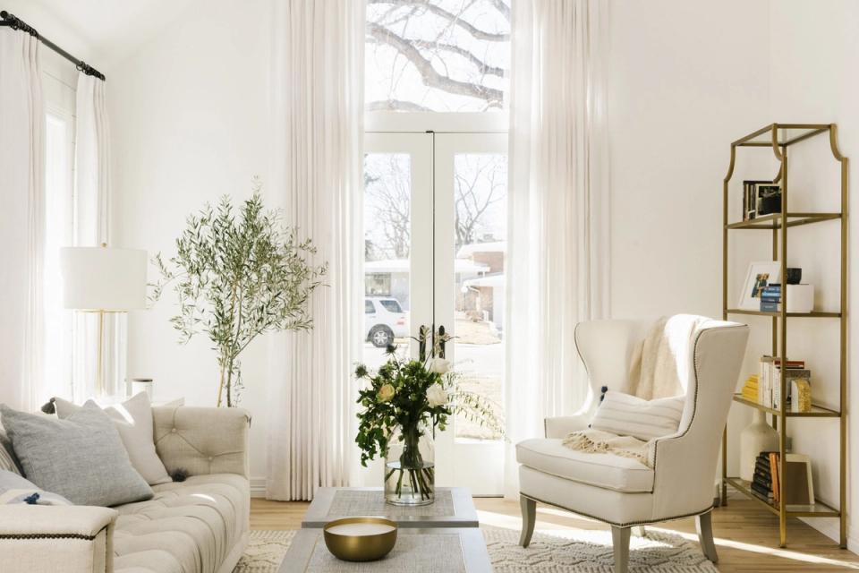 Bright minimalist living room with floor-to-ceiling curtains, cream furniture, and botanical accents