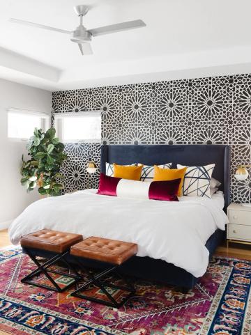 Eclectic bedroom with geometric patterned accent wall, jewel-tone pillows, and layered bohemian rugs