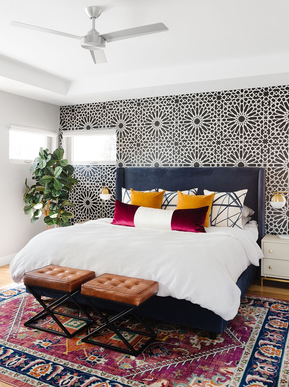 Eclectic bedroom with geometric patterned accent wall, jewel-tone pillows, and layered bohemian rugs