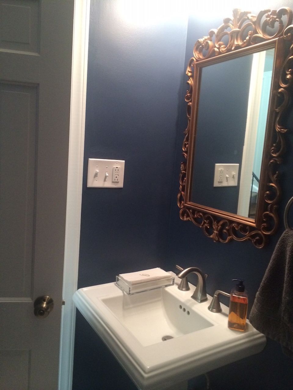Moody navy walls with ornate gold-framed mirror and white sink create an eclectic, dramatic powder room aesthetic.