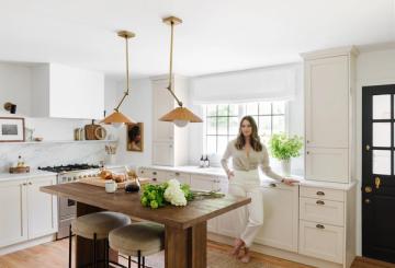 Bright farmhouse kitchen with white cabinetry, brass pendant lights, and rustic wood island