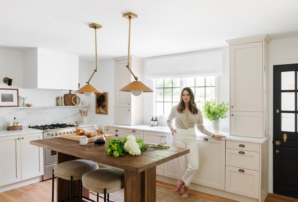 Bright farmhouse kitchen with white cabinetry, brass pendant lights, and rustic wood island