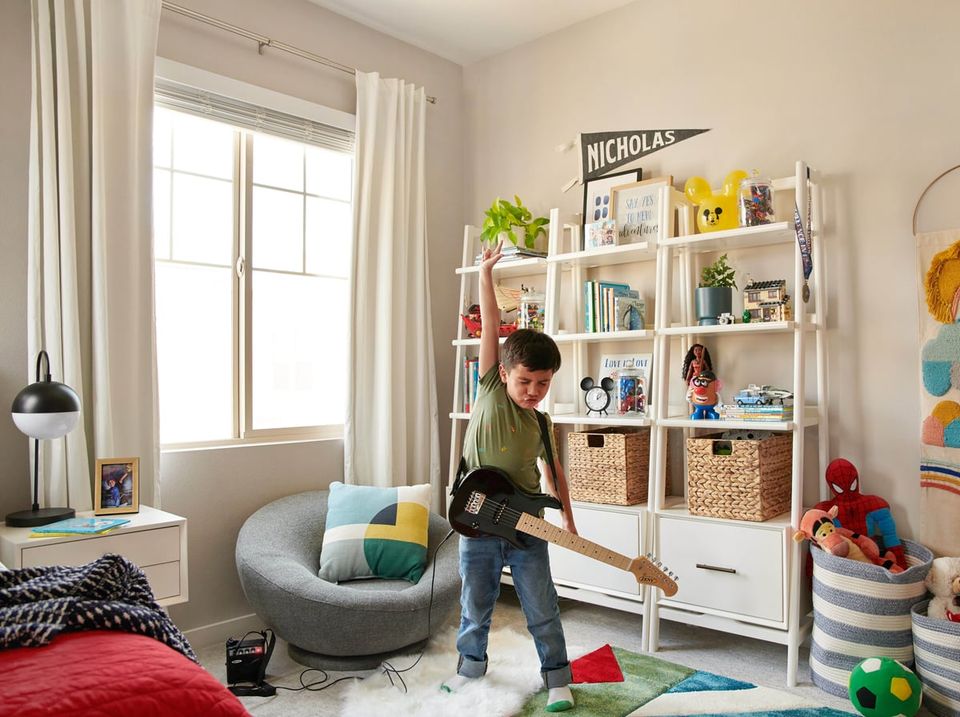 Bright, playful bedroom with neutral walls, white shelving, cozy gray chair, and colorful toy storage creating a functional, cheerful kid's space.