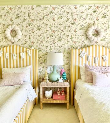 Bright maximalist twin bedroom with yellow striped headboards, floral wallpaper, and cheerful pastels