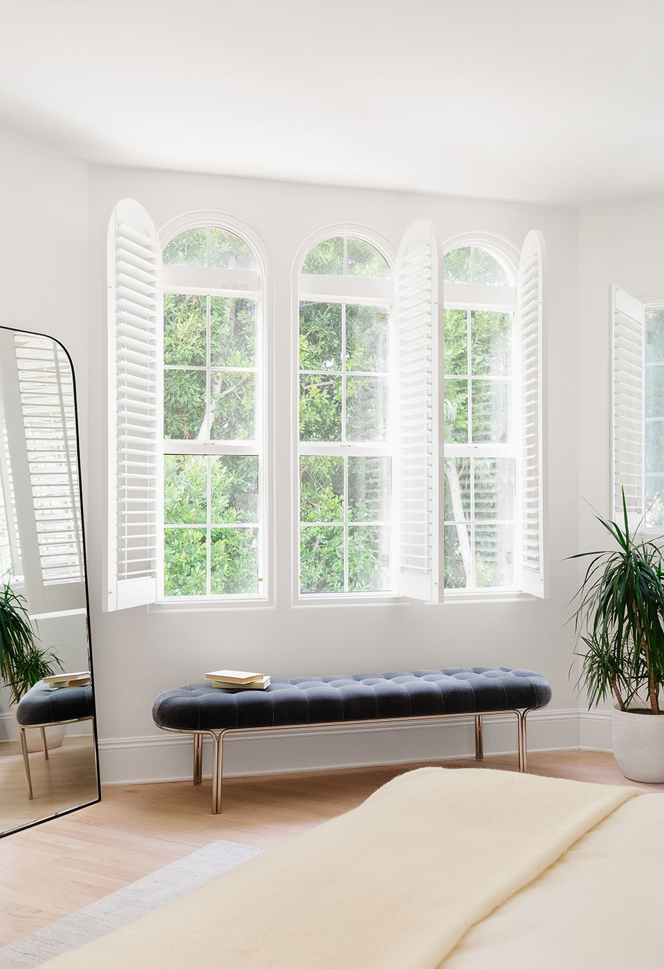 Modern minimalist bedroom with white plantation shutters, light wood floors, and neutral tones