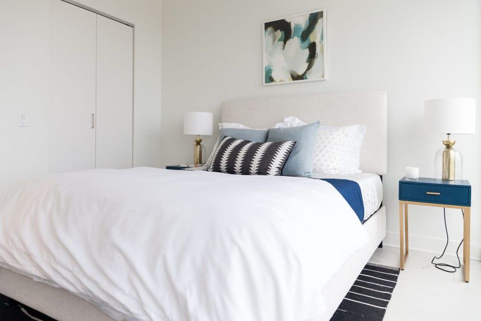 Modern minimalist bedroom with crisp white bedding, navy accents, and warm wood nightstands creating calm sophistication.