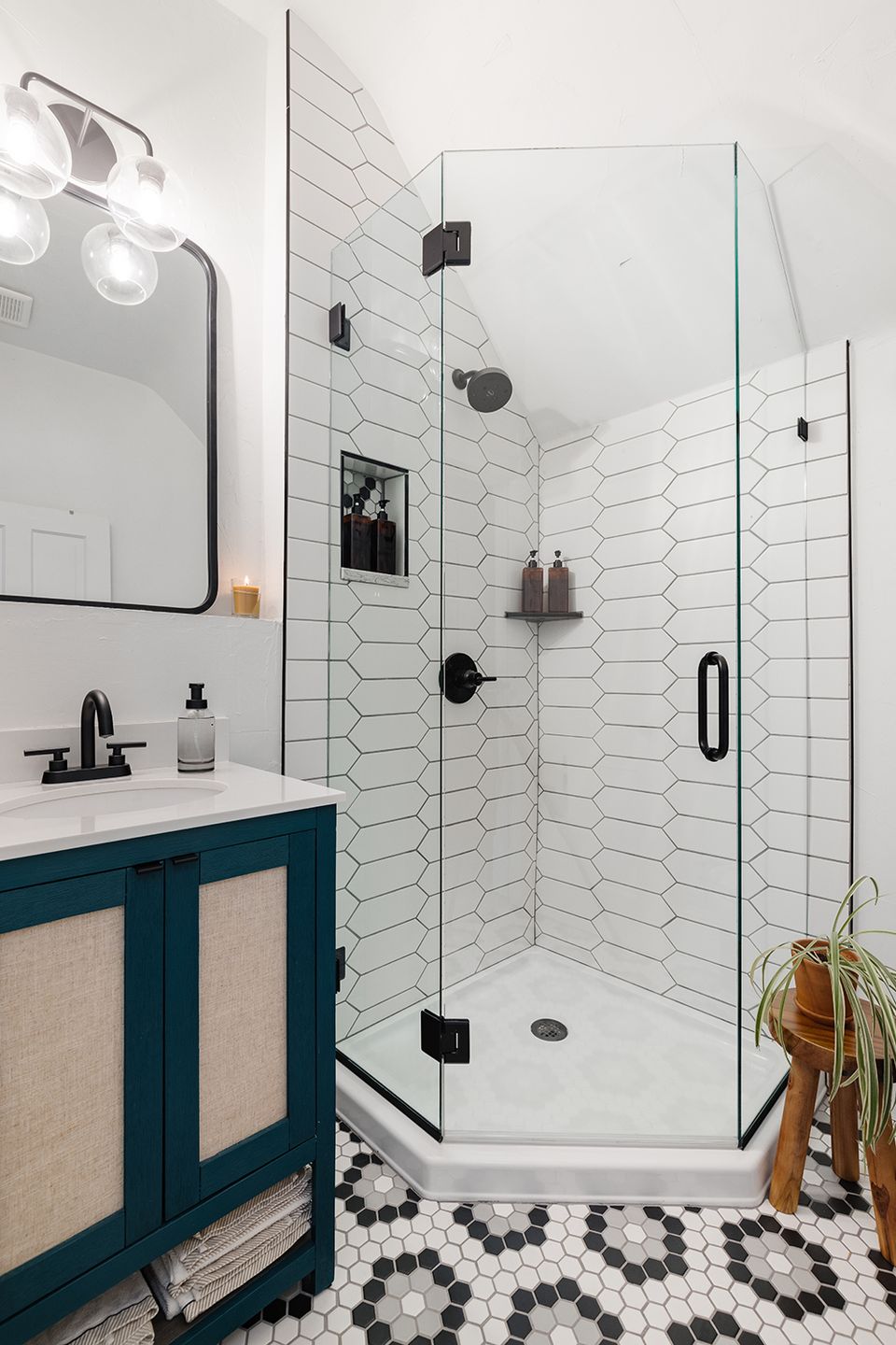Modern spa bathroom featuring chevron tile, teal vanity, and black-framed glass shower enclosure