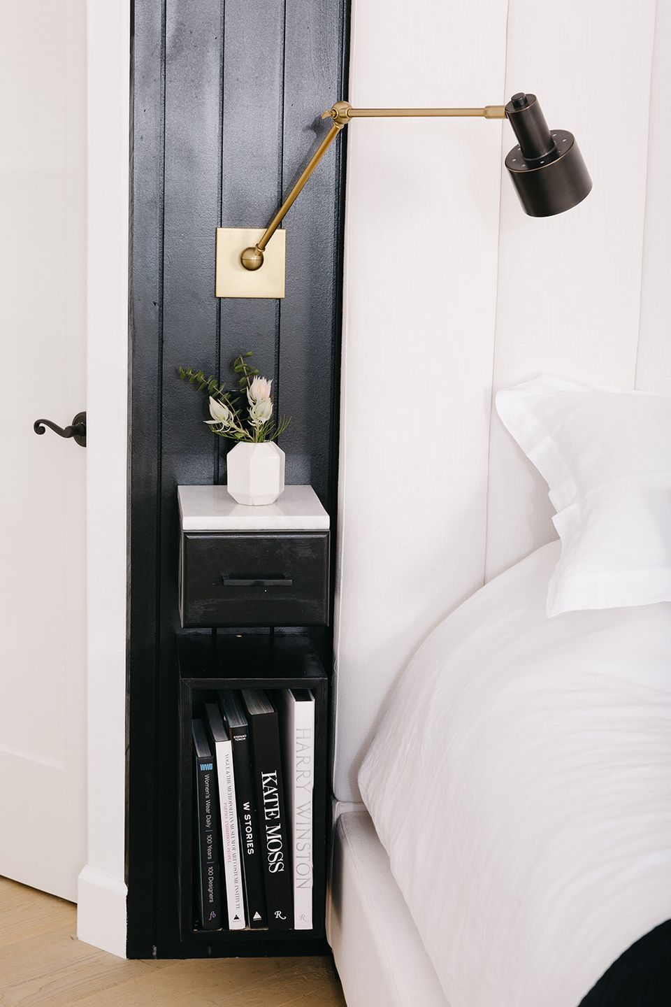 Modern minimalist bedroom with black built-in nightstand, brass articulating lamp, and crisp white bedding creating a sleek, contemporary aesthetic.