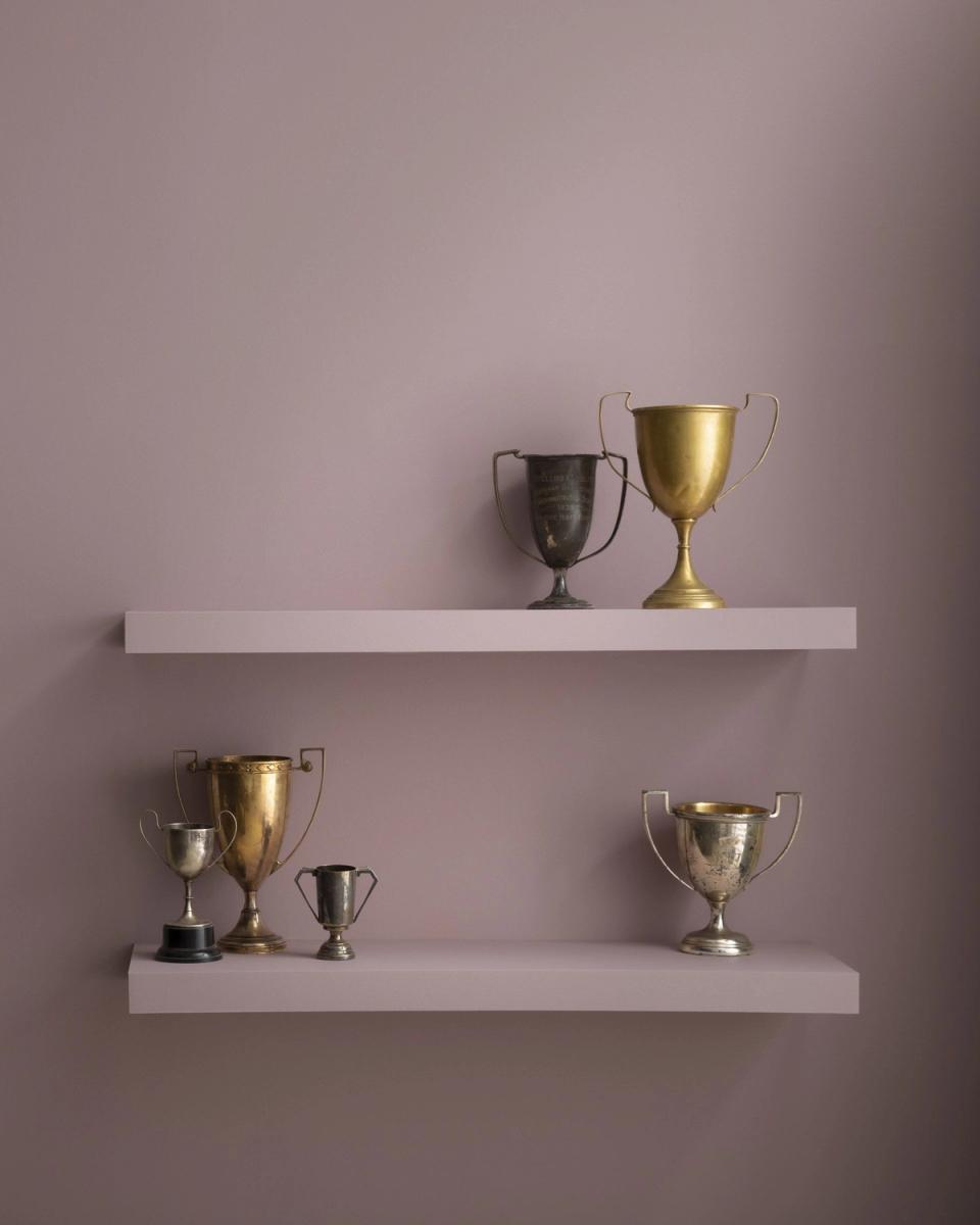 Warm mauve wall with tassel-trimmed linen pillow on white pedestal table beside black-framed window, coastal-inspired serene mood