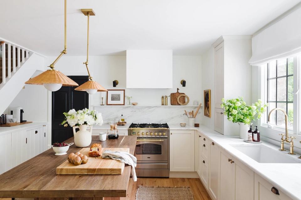Farmhouse kitchen blending white cabinetry, warm wood counters, brass pendant lights, and minimalist open shelving