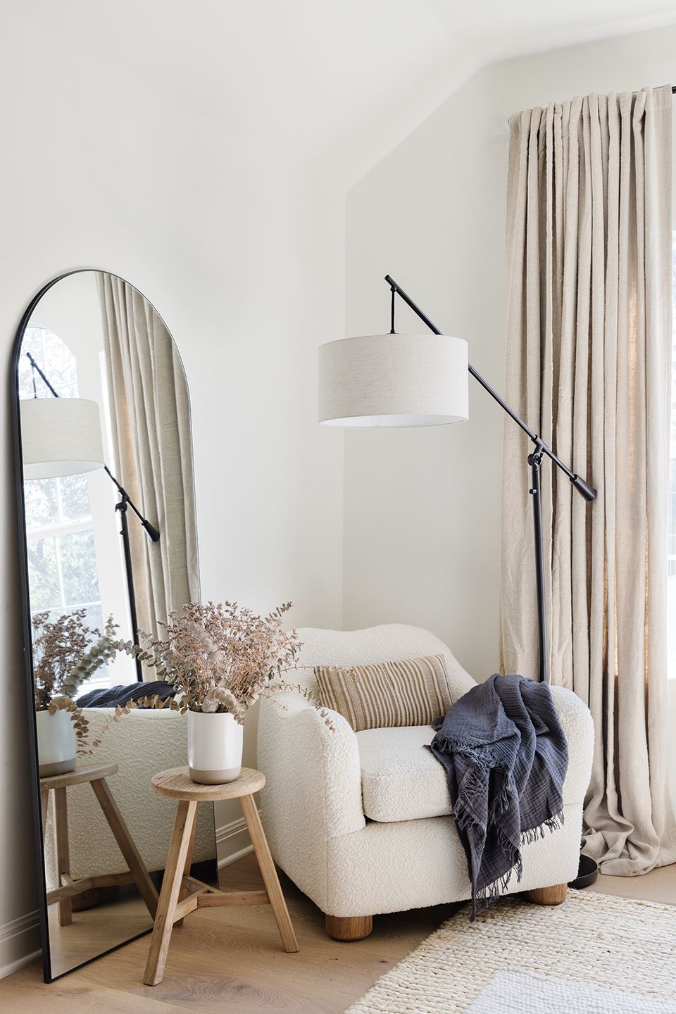 Serene minimalist bedroom corner with cream chair, arched mirror, and neutral linen drapes