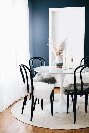Sophisticated round white dining table with black bentwood chairs against deep teal accent wall and modern white panel backdrop