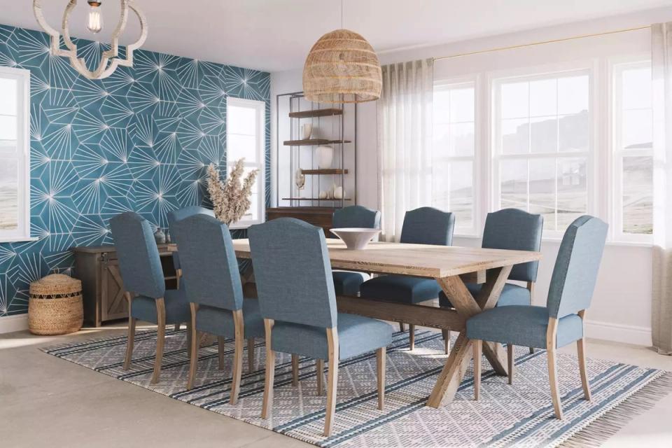 Bright coastal dining room with teal botanical wallpaper accent, natural wood table, and blue-gray chairs