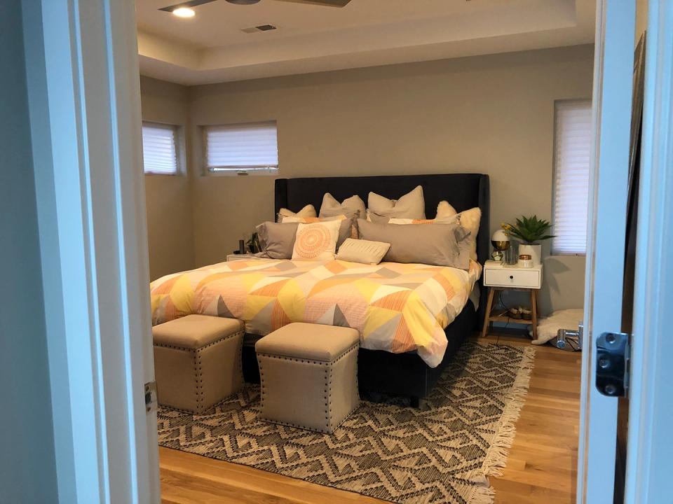 Warm contemporary bedroom with yellow geometric bedding, taupe walls, nailhead ottomans, and soft ambient lighting