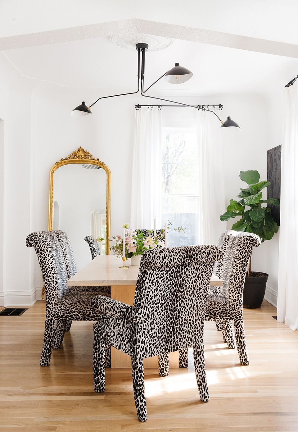 Modern eclectic dining nook with animal-print chairs, brass mirror, sculptural black lighting, and botanical touches creating playful sophistication.
