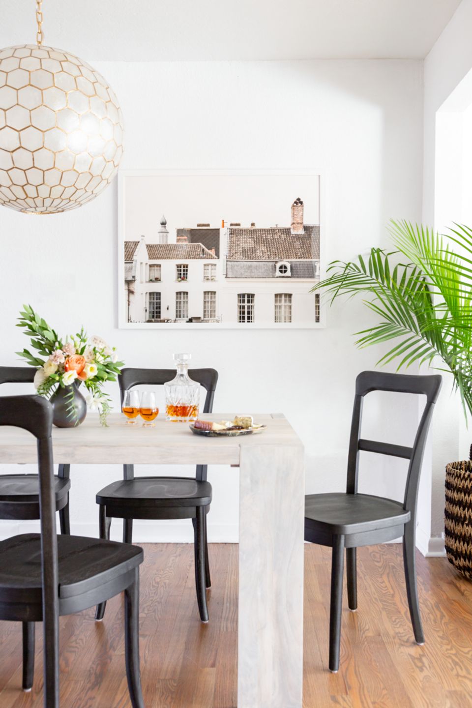 Modern dining space with Parisian architecture art, natural plants, and black chairs.