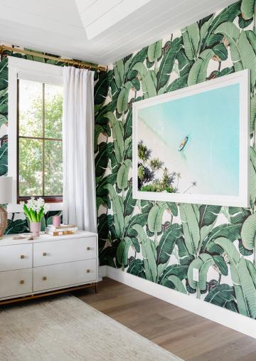 Tropical botanical bedroom with oversized turquoise coastal landscape art on leafy wallpaper
