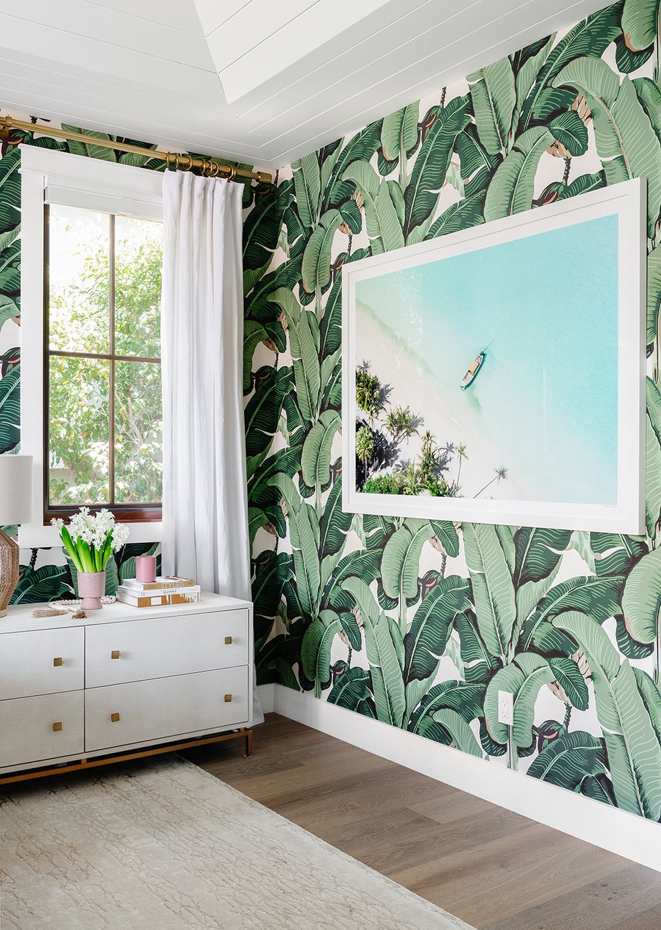 Tropical botanical bedroom with oversized turquoise coastal landscape art on leafy wallpaper