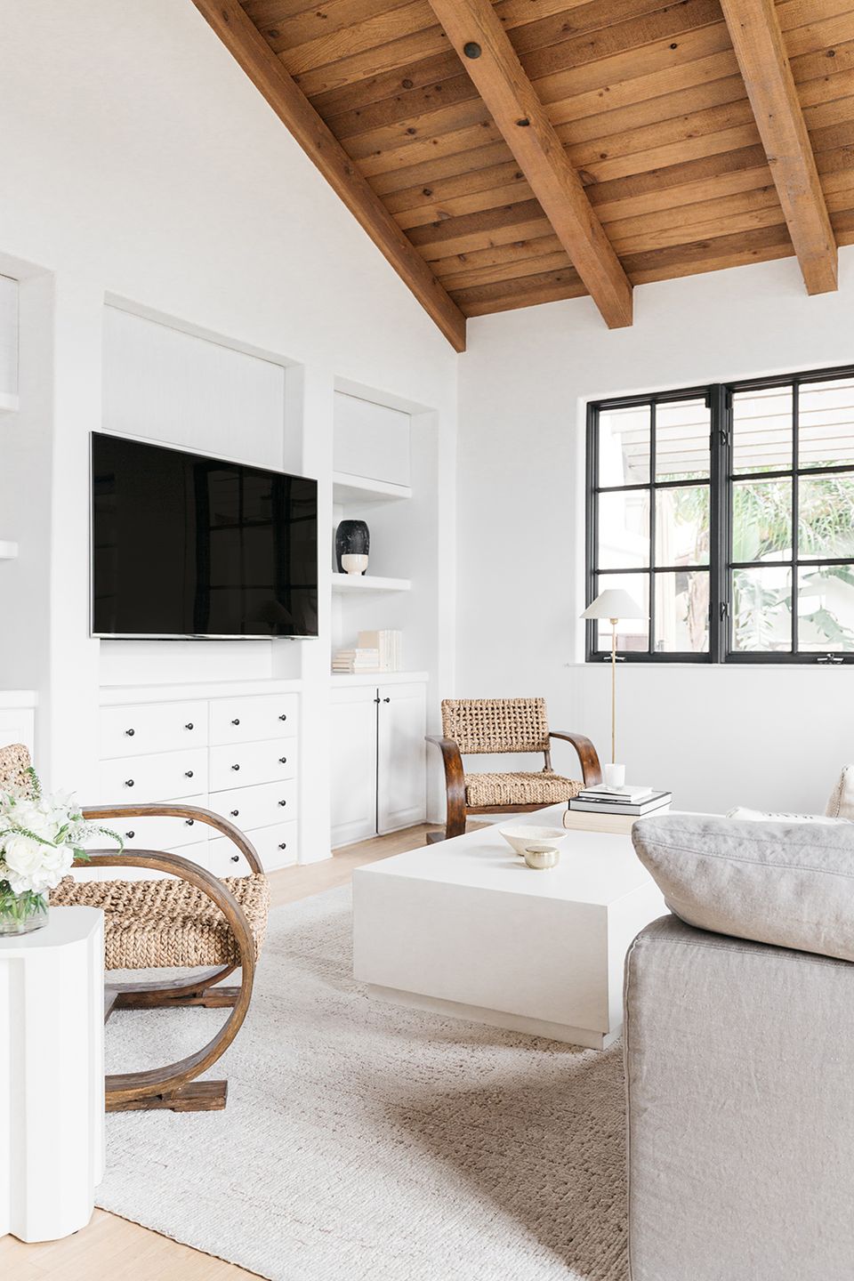 Bright farmhouse bedroom with white TV cabinet, exposed wood ceiling, and natural textures