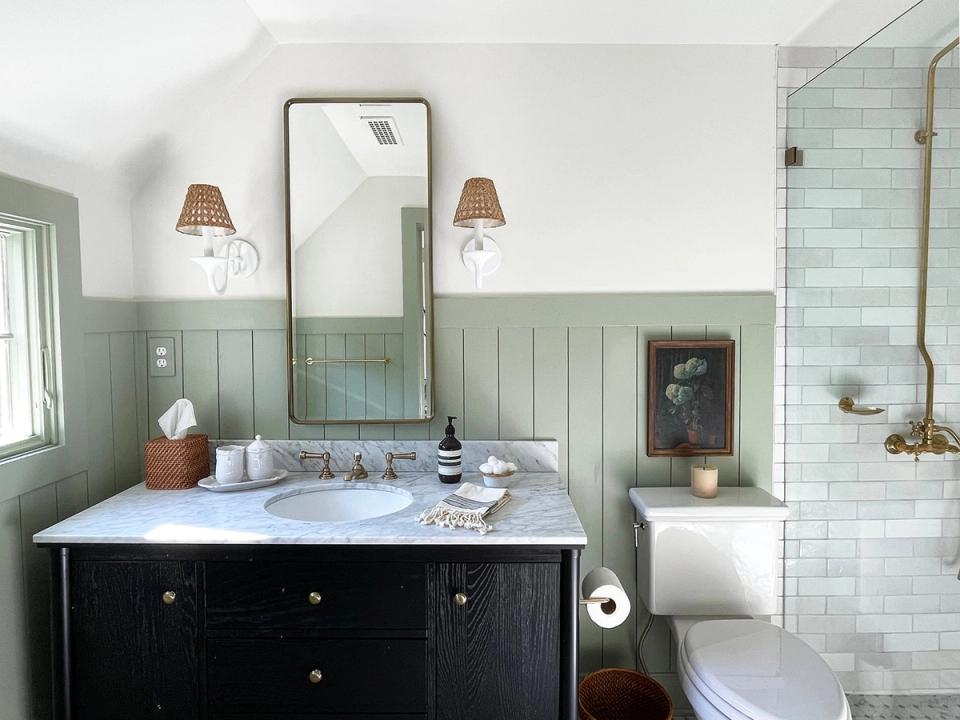 Spa-like farmhouse bathroom with sage green wainscoting, black vanity, marble countertop, and soft brass sconces