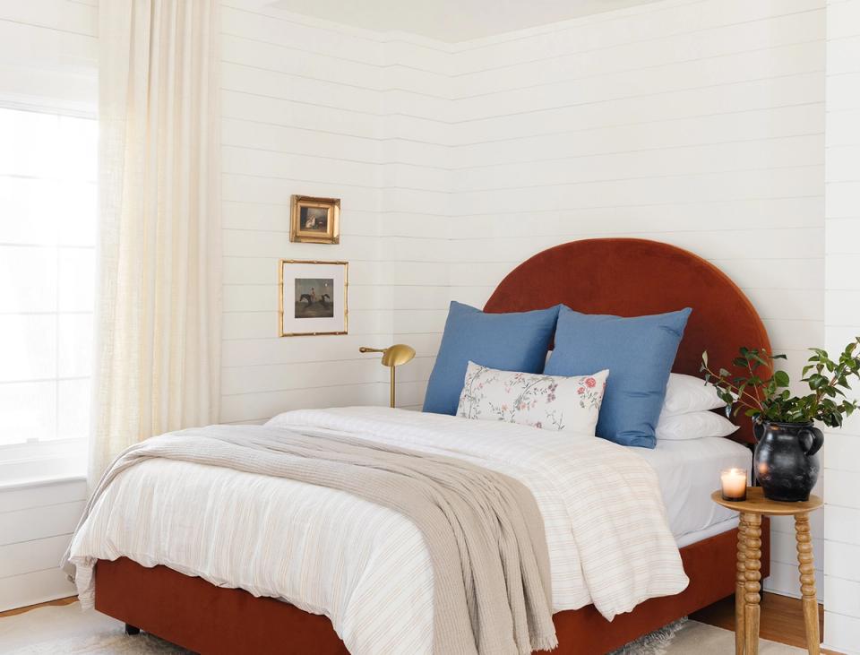Serene bedroom with rust-red velvet headboard, blue pillows, and cream bedding.