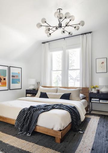Mid-century modern bedroom with natural wood frame, geometric rug, and sculptural ceiling light