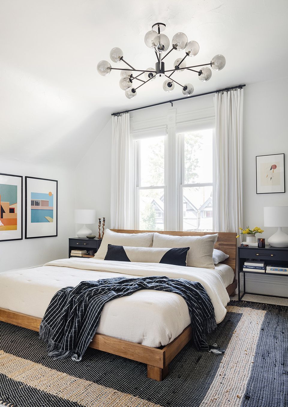 Mid-century modern bedroom with natural wood frame, geometric rug, and sculptural ceiling light