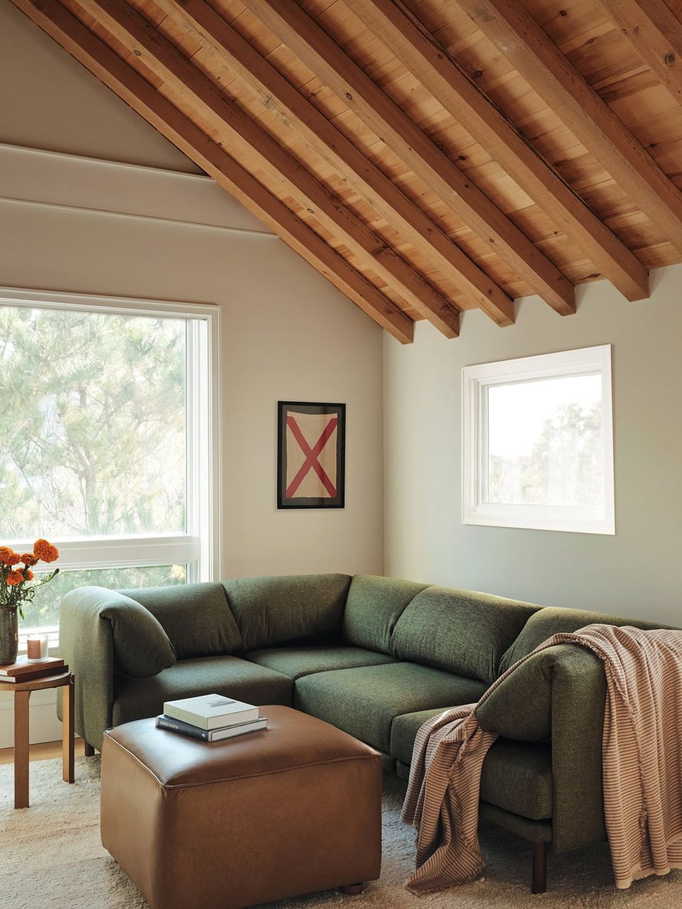 Rustic farmhouse lounge with sage green sectional, exposed wood beams, and warm earthy tones throughout.
