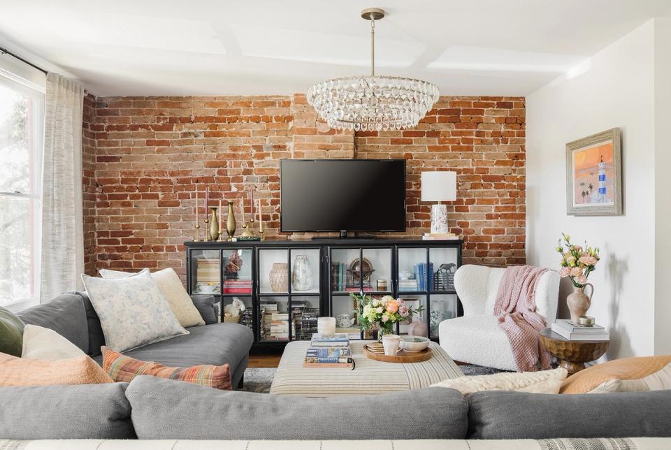 Contemporary living room with exposed brick, gray sofa, modular storage, and warm lighting creating inviting, grounded atmosphere.