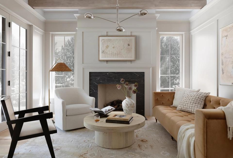 Modern living room with warm neutrals, black fireplace, caramel leather sofa, and natural light from large windows