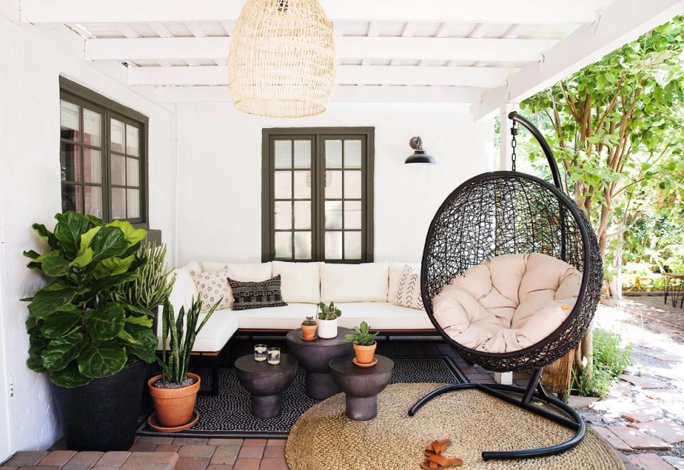 Bright bohemian patio with woven rattan hanging chair, potted plants, and natural textures creating a relaxed coastal retreat.