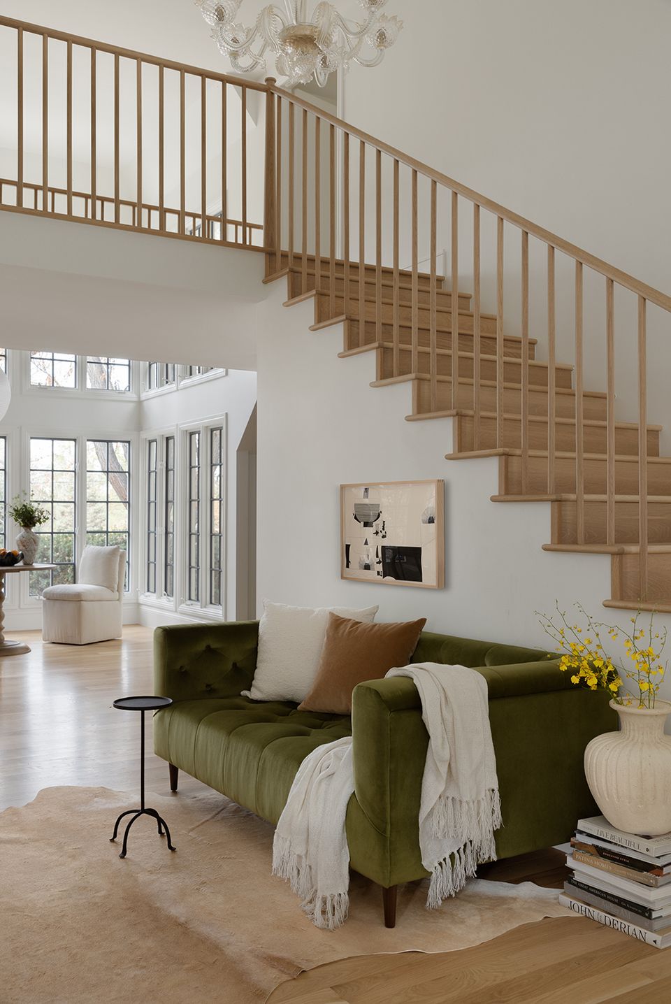 Bright minimalist living room with sage green velvet sofa, warm wood staircase, and neutral palette creating serene, airy atmosphere