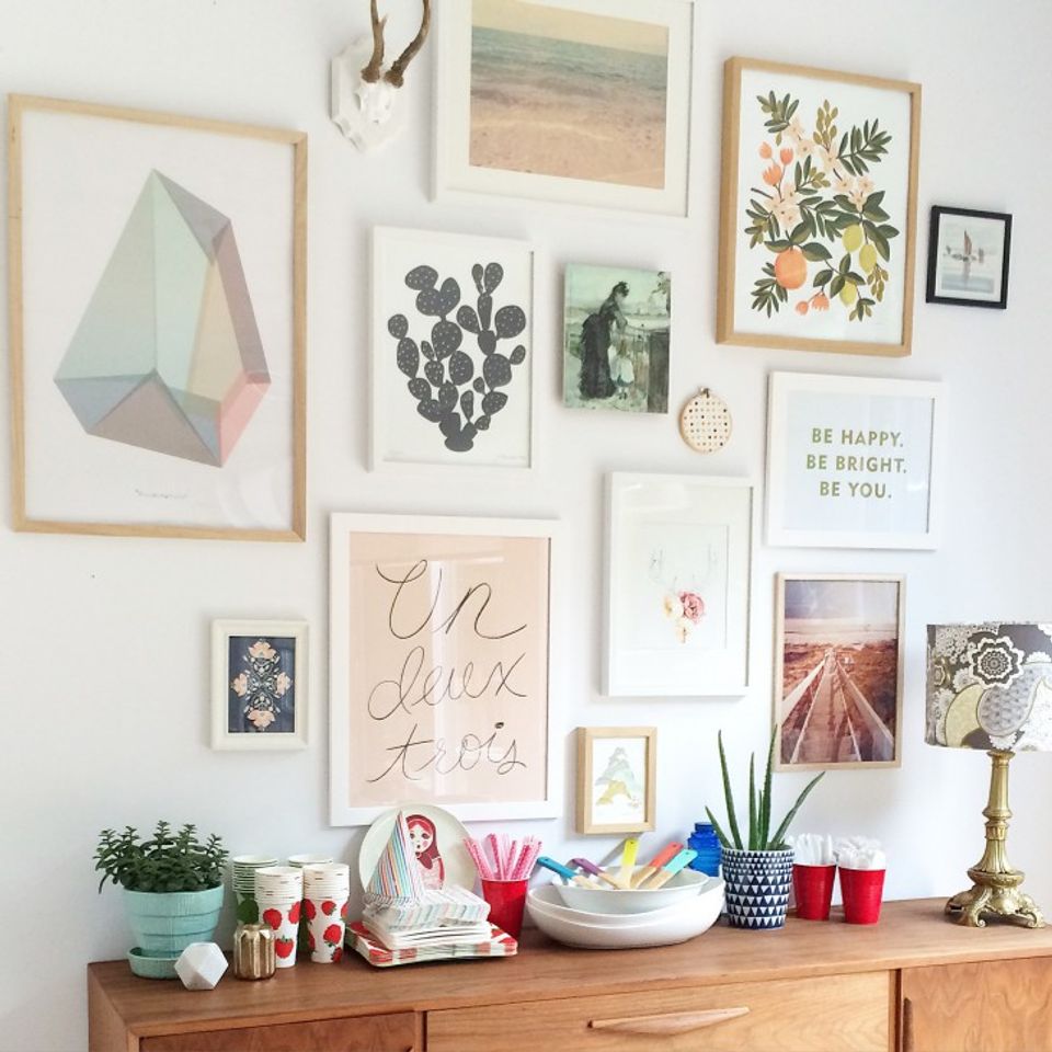 Gallery wall with mixed-frame botanical and geometric art above wooden desk with plants