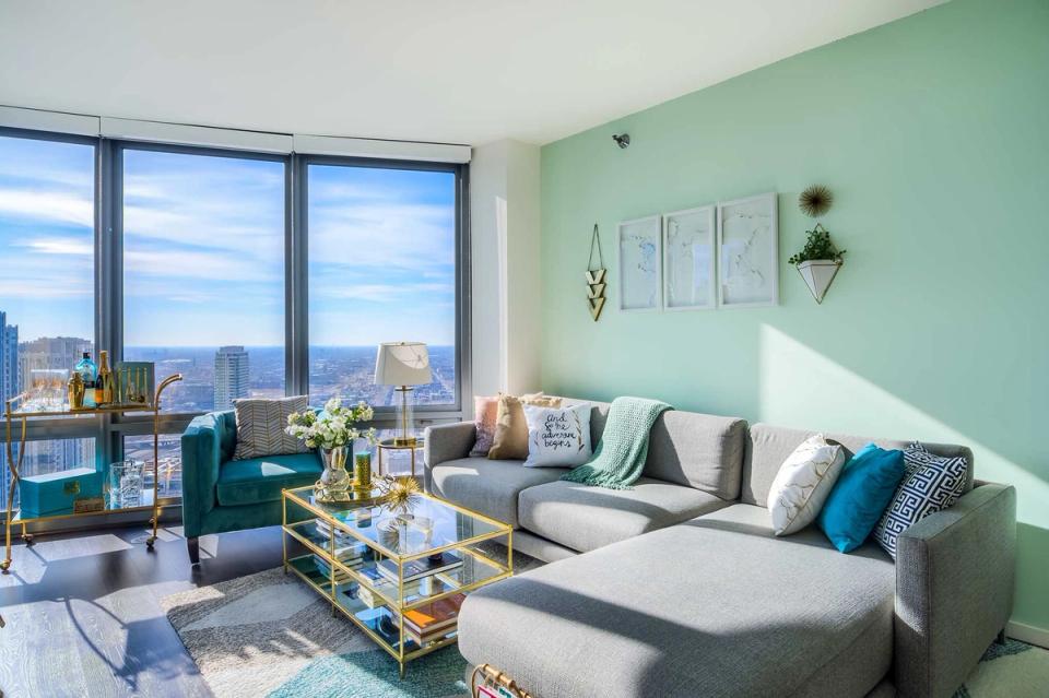 Bright modern living room with mint green accent wall, gray sectional, and cityscape views from floor-to-ceiling windows