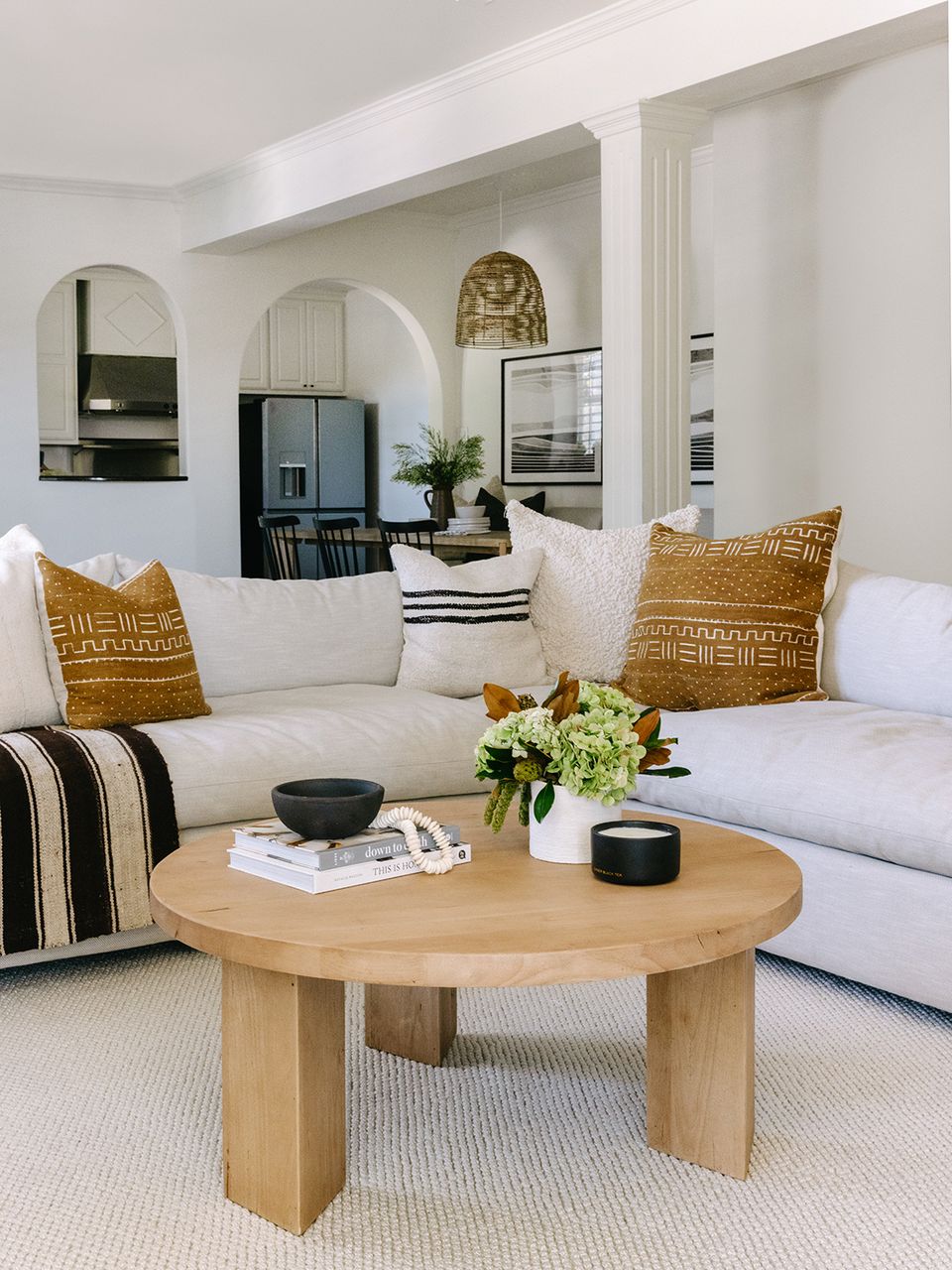 Airy organic modern lounge with curved arches, cream sectional, natural wood table, and mustard accent pillows