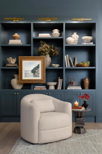 Modern eclectic shelving with teal-blue cabinetry, brass lighting, and curated art collection