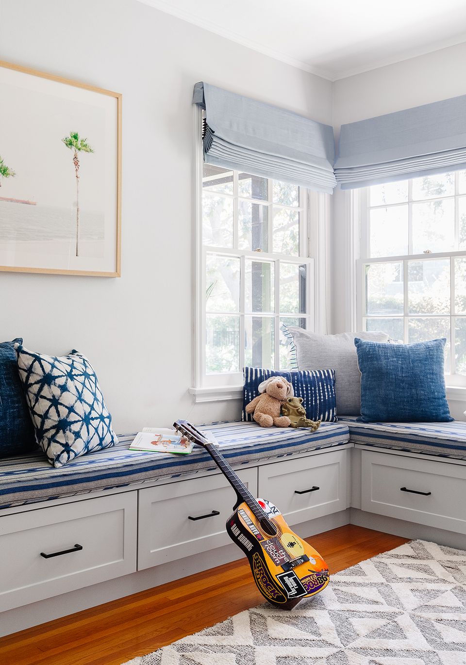 Modern window seat with blue-and-white striped cushion, drawers, and geometric pillows for organized, coastal-style storage.