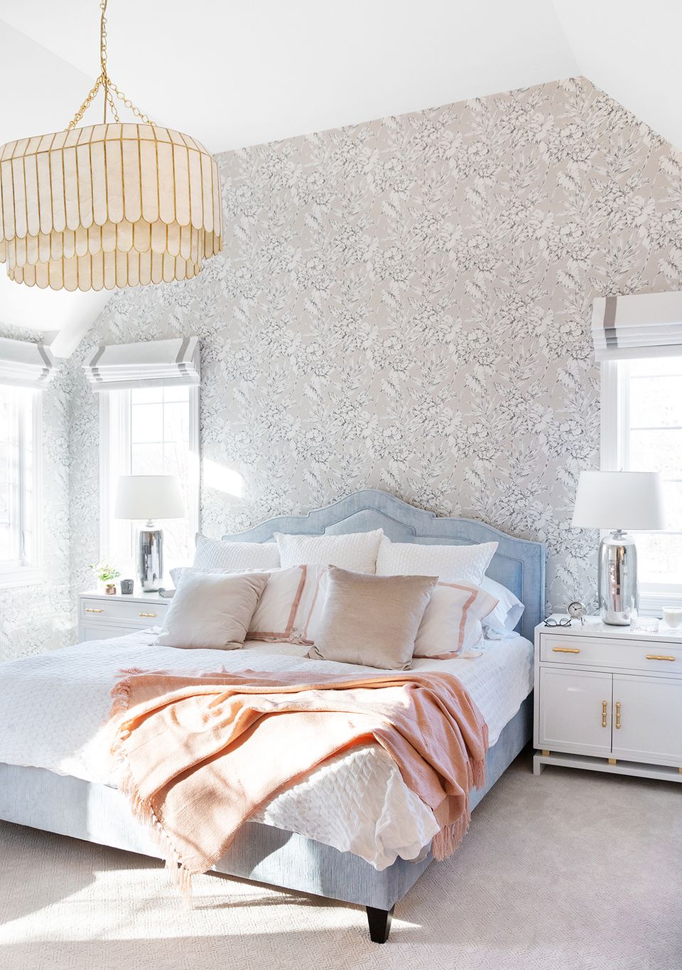 Soft, feminine bedroom with blue upholstered headboard, patterned wallpaper accent wall, and warm peachy tones throughout