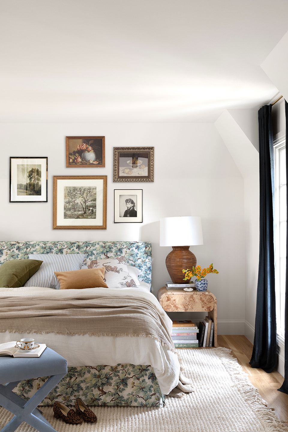Bohemian bedroom with blue floral headboard, gallery wall, and natural wood nightstand