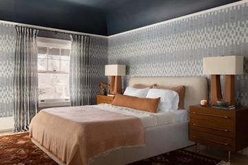 Contemporary bedroom with dramatic dark blue ceiling, patterned wallpaper, warm wood nightstands, and neutral bedding