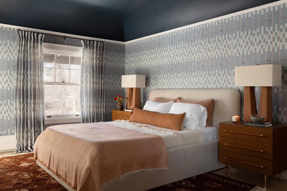 Sophisticated bedroom with dramatic dark ceiling, geometric patterned wallpaper, rich wood nightstands, and warm peachy-gold bedding for layered elegance.