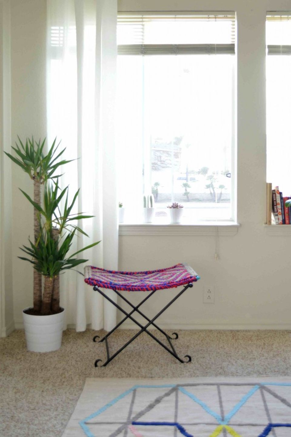 Bright coastal nook with potted palm, geometric rug, and purple woven seat near sunlit windows