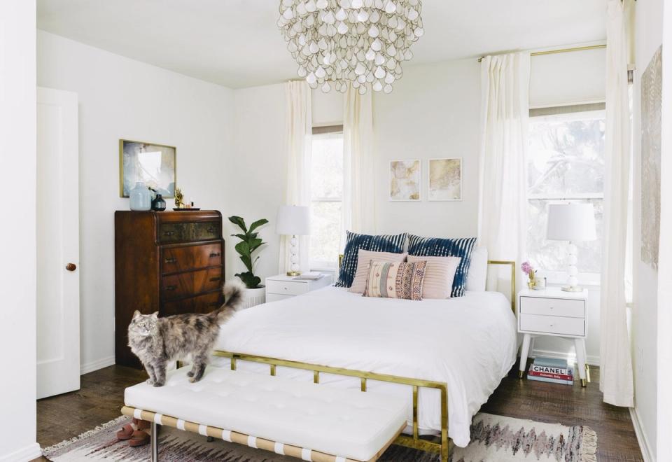 Bright transitional bedroom with white walls, brass bed frame, navy accents, and crystal chandelier creating an airy, sophisticated retreat.