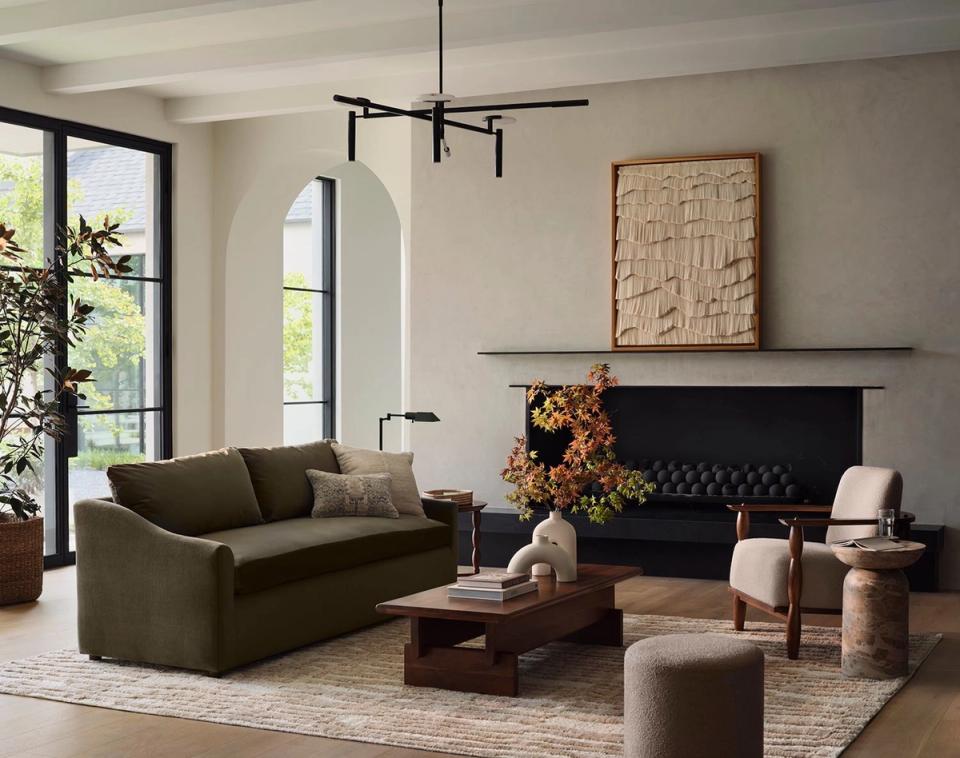 Modern living room with warm neutrals, olive sectional, and black fireplace mantel balanced with natural light and greenery