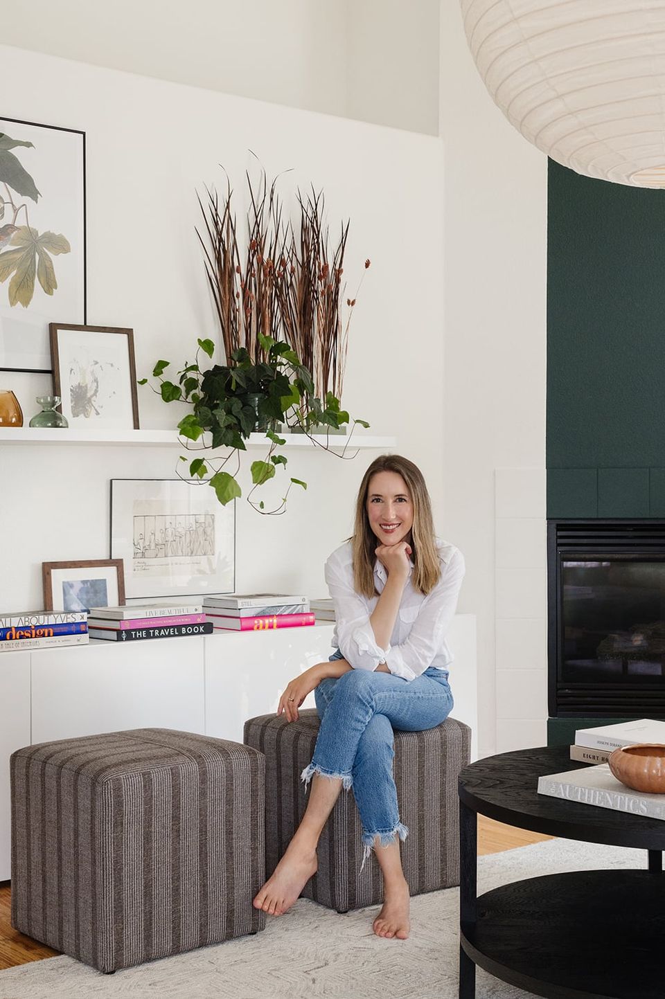 Modern living corner featuring white shelving with plants and art, striped poufs, dark fireplace accent wall