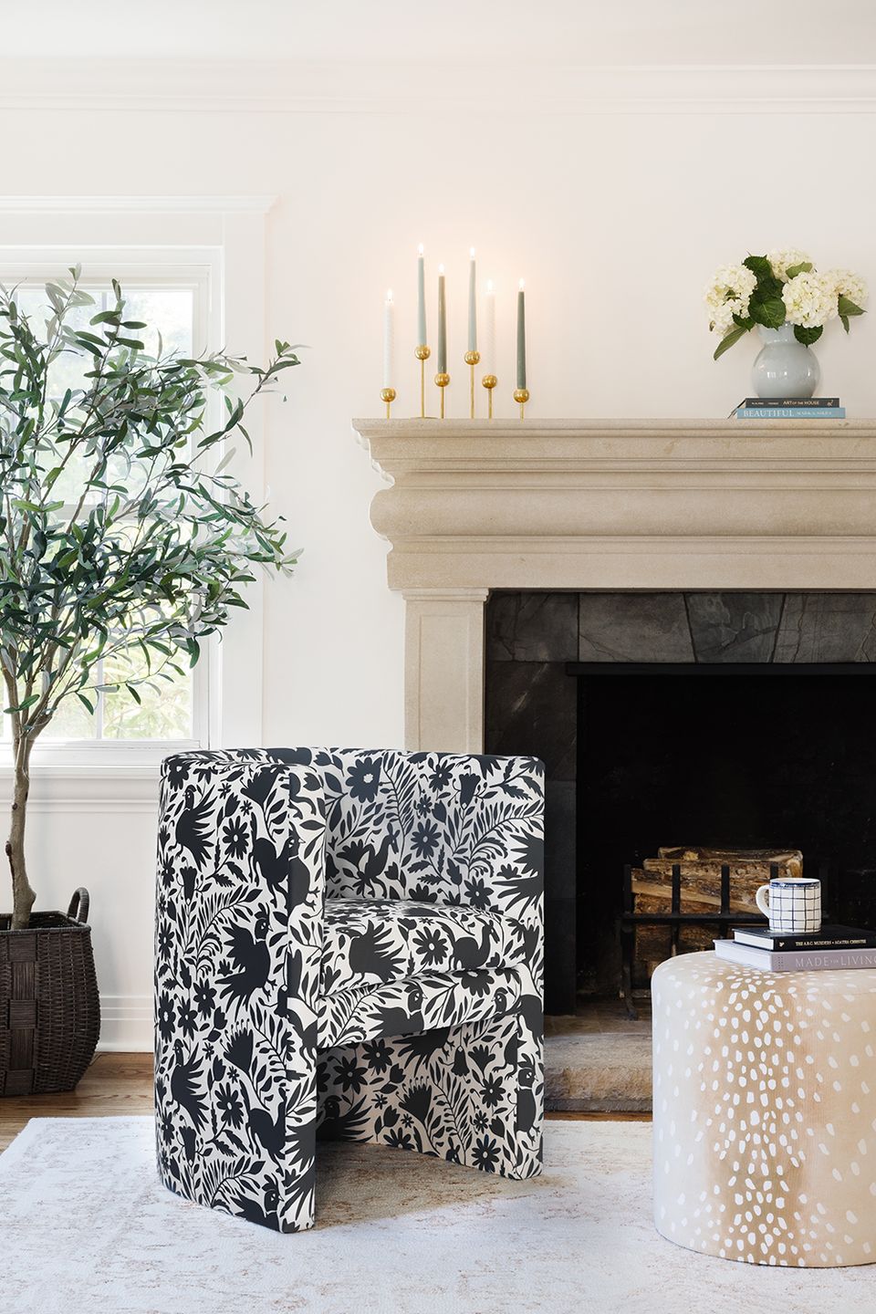 Elegant fireplace mantel with cream molding, brass candlesticks, and black botanical-print accent chair